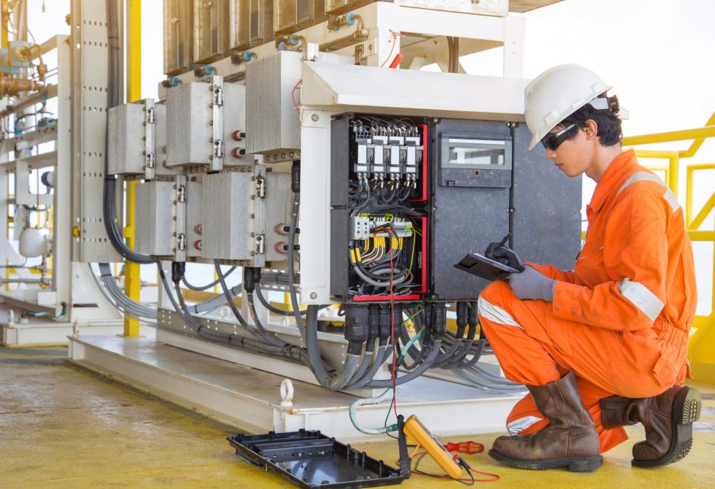 Electrical and instrument technician measuring voltage of thermo electric generator and record reading value to maintenance sheet for annual inspection at offshore oil and gas remote platform.